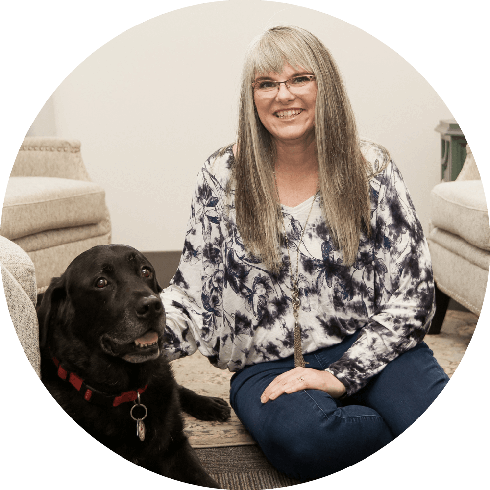 Liane Wood, who offers clinical supervision, sitting in her counselling office with her black lab dog by her side
